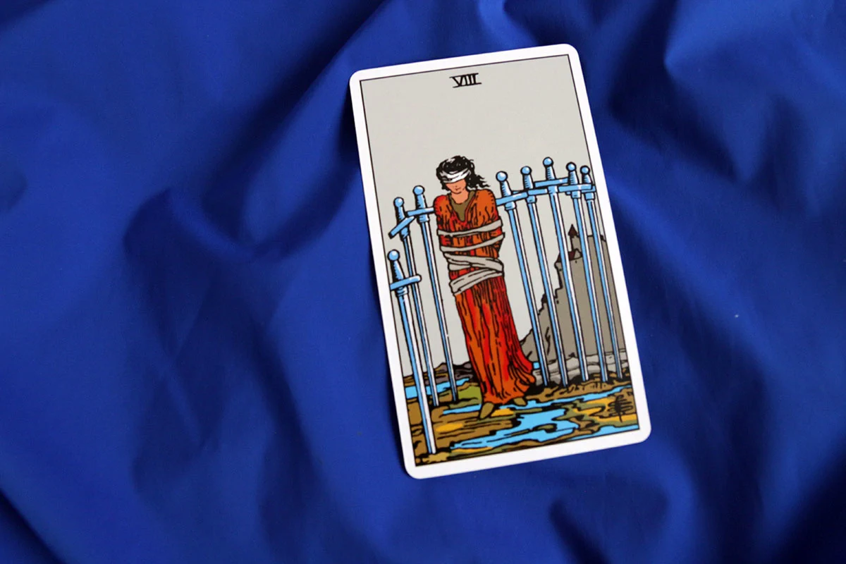 Karta tarota „Ósemka Mieczy” z talii Rider–Waite–Smith na niebieskim tle.