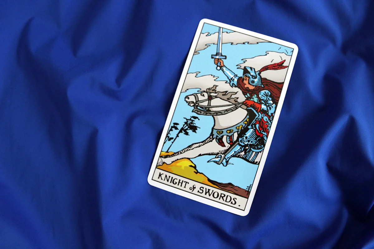 Karta tarota „Rycerz Mieczy” z talii Rider–Waite–Smith na niebieskim tle.